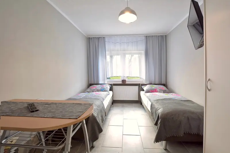 Apartament 1 – pokój z dwoma łóżkami pojedynczymi, stolikiem i telewizorem na ścianie