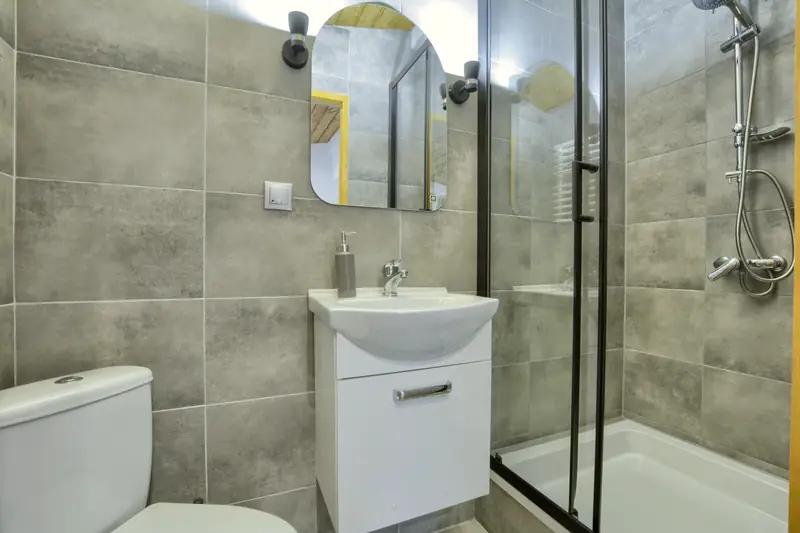 Apartament 4 – łazienka z szarymi płytkami i kabiną prysznicową w czarnej ramie