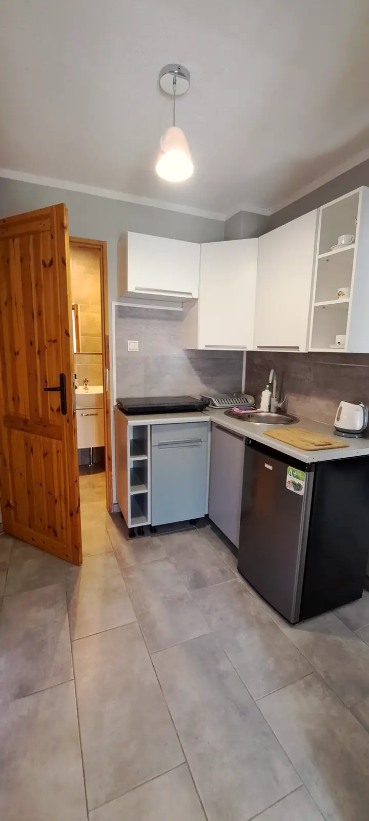 Apartament 1 – aneks kuchenny z białymi szafkami i małą lodówką