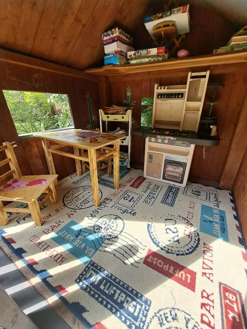 Wnętrze drewnianego domku dla dzieci ze stolikiem, krzesełkami, kuchenką do zabawy i grami planszowymi