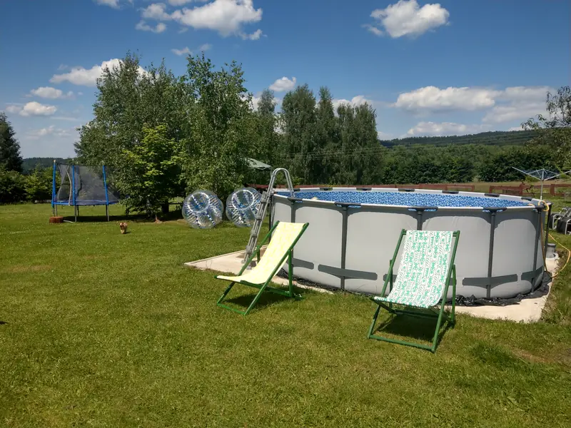 Okrągły basen stelażowy z leżakami na trawniku, obok kule do zorbingu i trampolina
