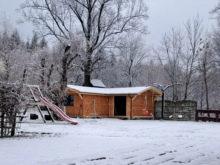 Drewniana wiata z huśtawkami i zjeżdżalnia pod śniegiem, w tle oszronione drzewa